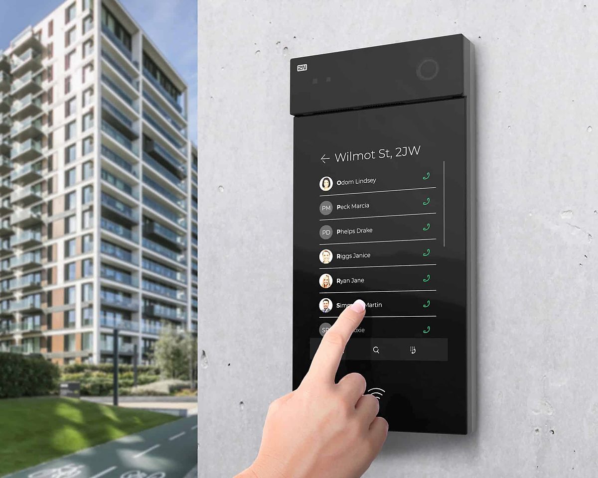 Person using a touchscreen video intercom at the entrance of an apartment tower