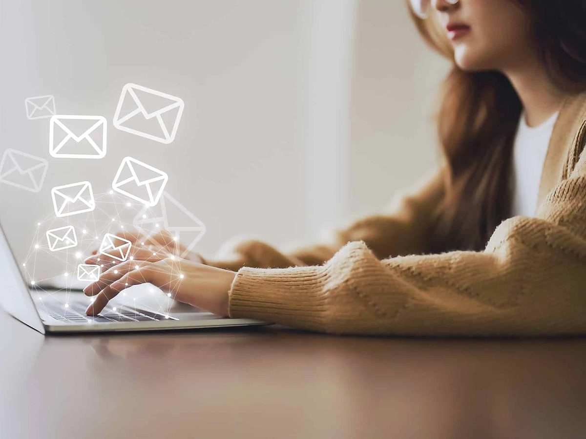 Person typing on a laptop with email icons floating above the keyboard
